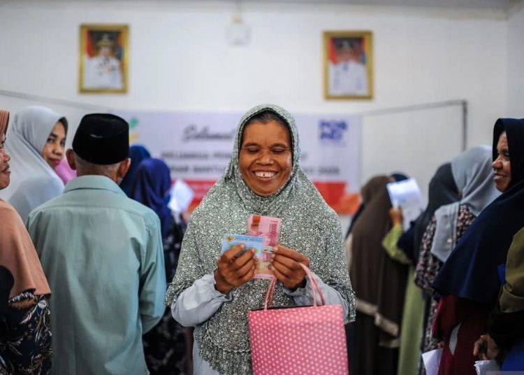 Seorang warga penerima bantuan menunjukkan uang bansos Program Keluarga Harapan (PKH) di Kantor Kecamatan Ciomas, Kabupaten, Serang, Banten, Selasa (25/2/2025).